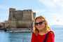Turista posando com Castel dell'Ovo ao fundo, na costa de Nápoles